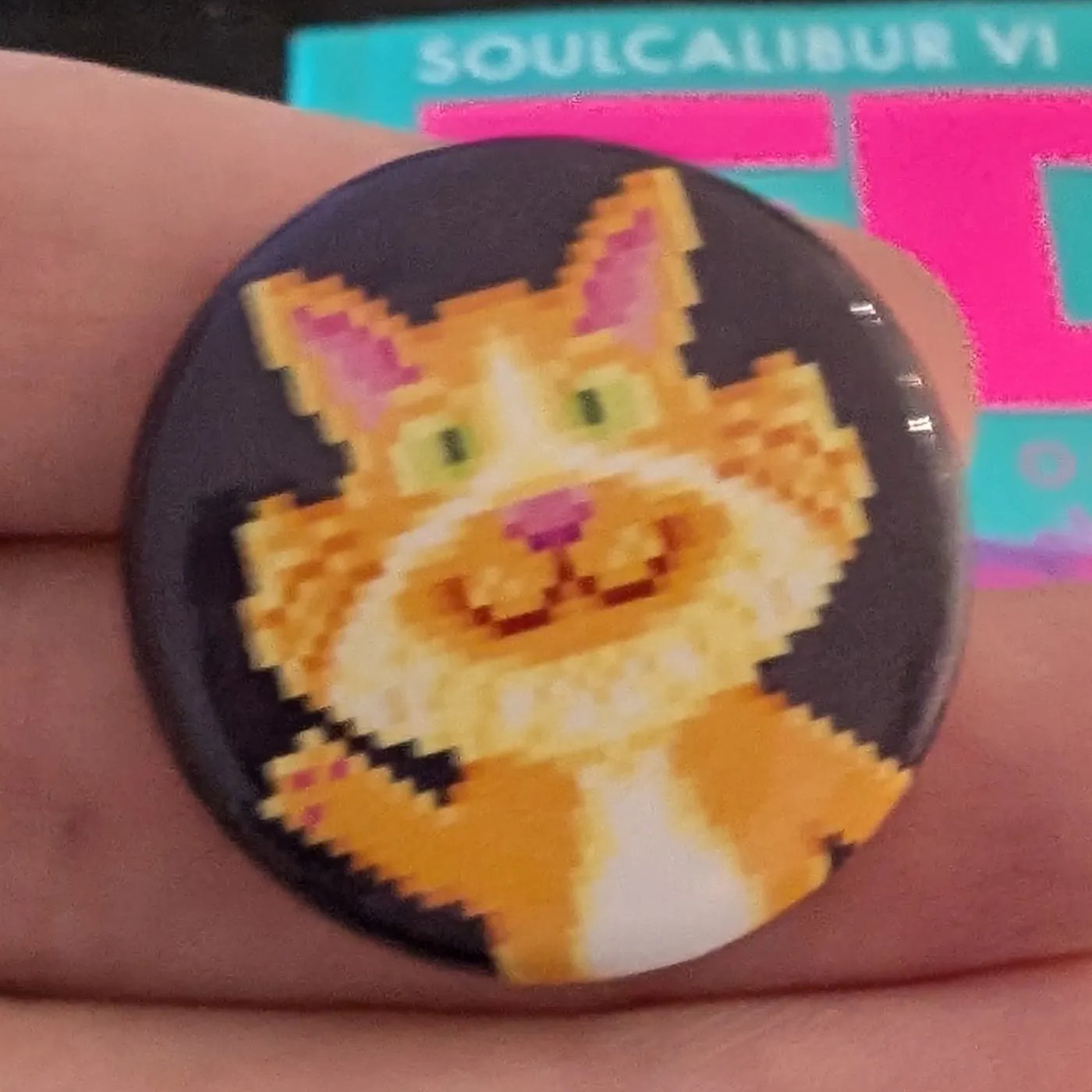 Pixel art pin badge of a grinning ginger and white cat waving